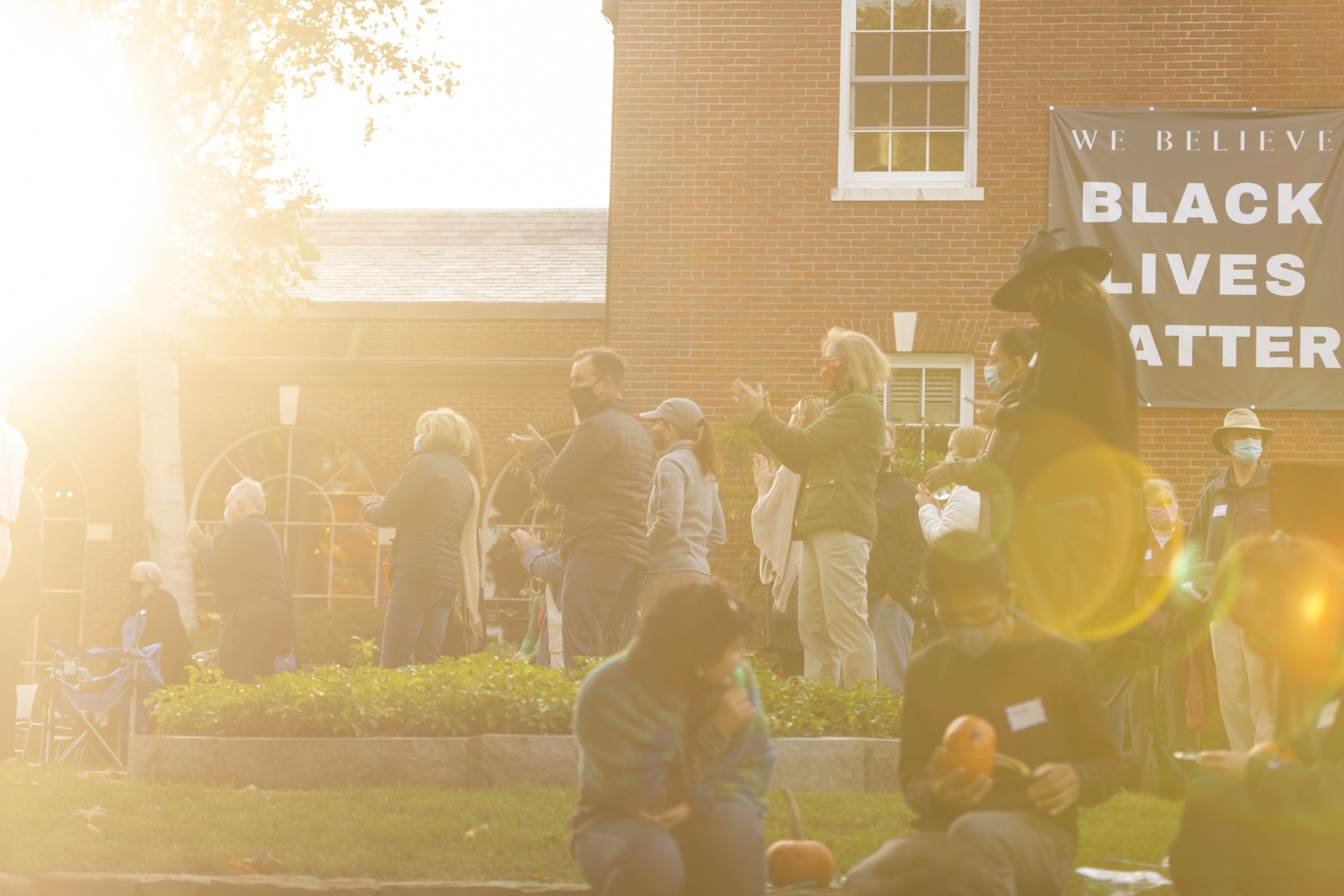 A group of people on the church lawn clapping. A Black Lives Matter sign is in the background.